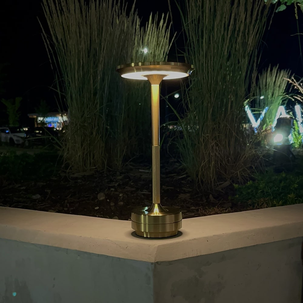 Brass cordless table lamp illuminating a garden area at night, ideal for outdoor use.