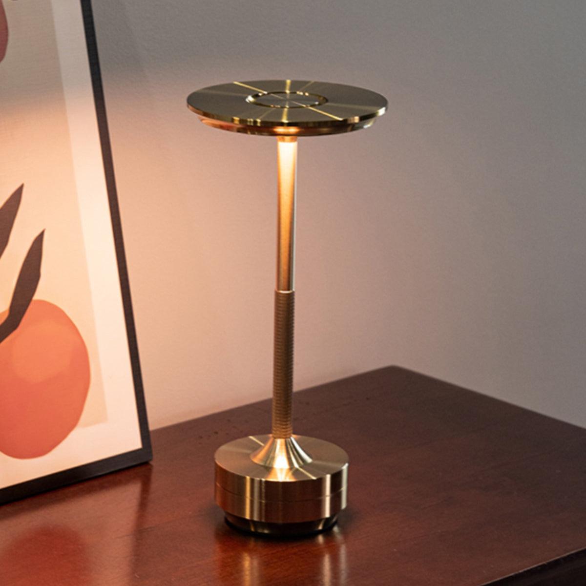 Sleek brass cordless table lamp with adjustable LED light on a wooden surface, suitable for home or office.