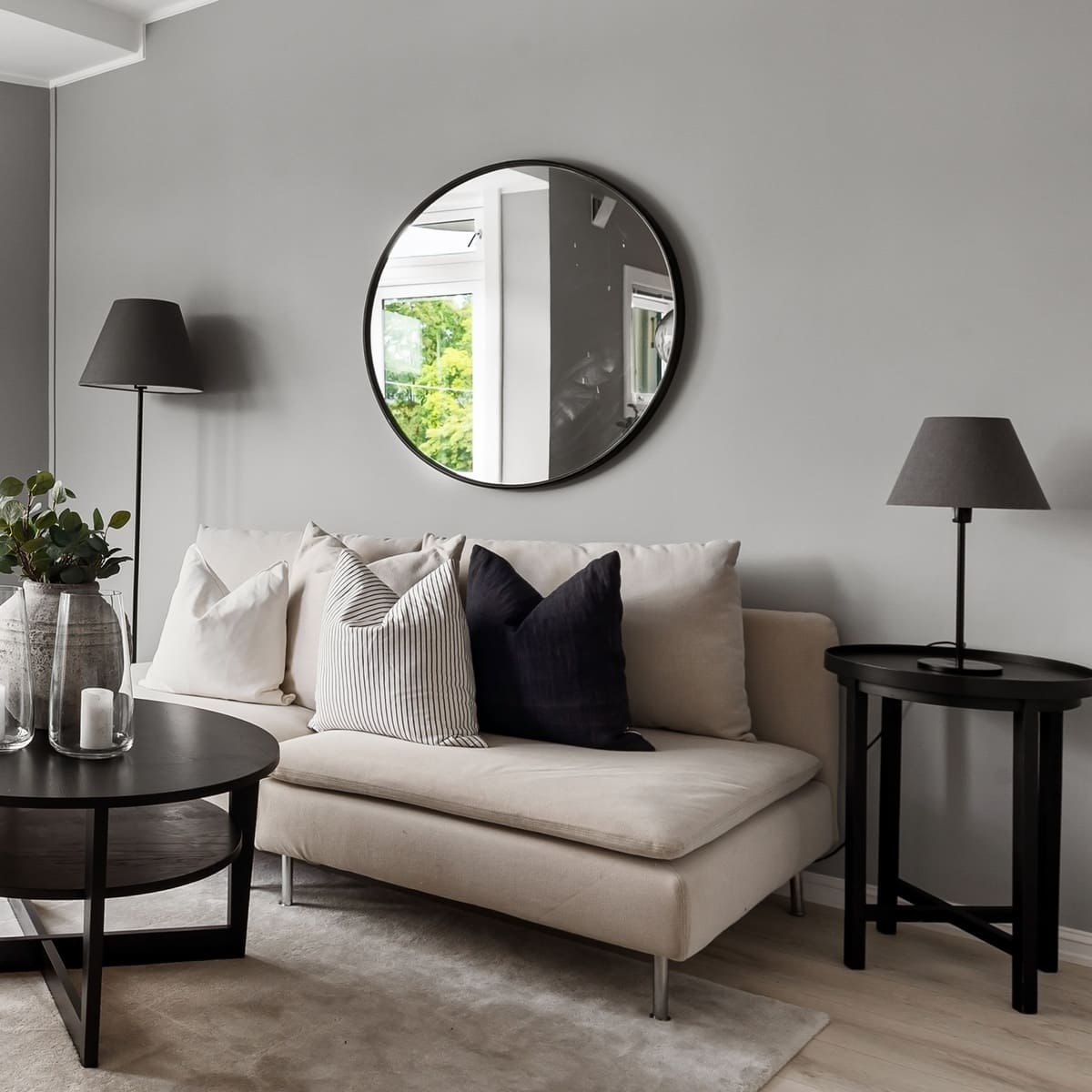 A modern living room featuring a beige sofa, a round mirror, and stylish black floor and table lamps.