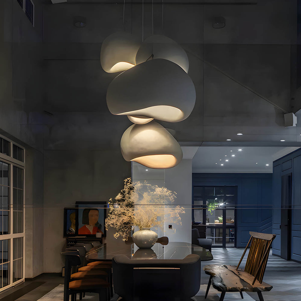 Cluster of minimalist chandeliers hanging over a dining area, featuring a wabi-sabi design with asymmetrical dome-shaped shades and warm lighting.