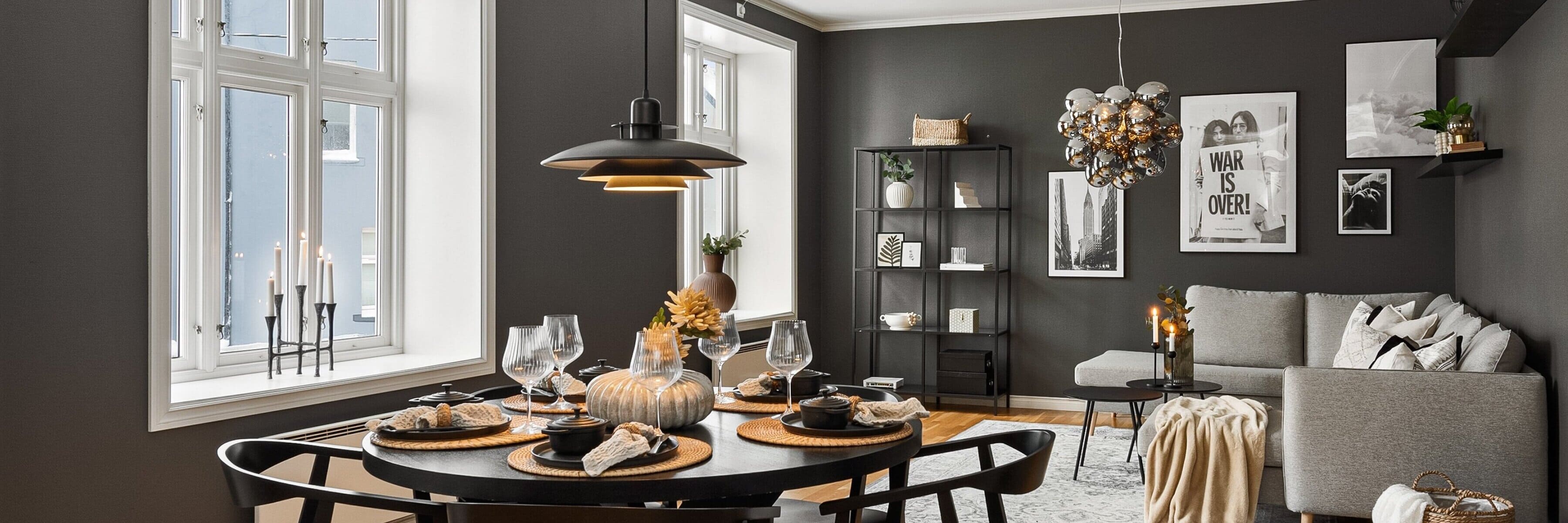 A contemporary dining room featuring a sleek black table with modern place settings, complemented by elegant pendant lights and a decorative glass chandelier against a dark gray wall backdrop.