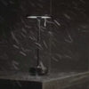 A cordless table lamp standing in heavy rain, demonstrating its water-resistant design for outdoor use.