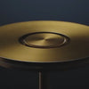 A close-up showcase of a brass cordless table lamp, highlighting the touch-sensitive top, sleek design, textured stem, and USB charging port.