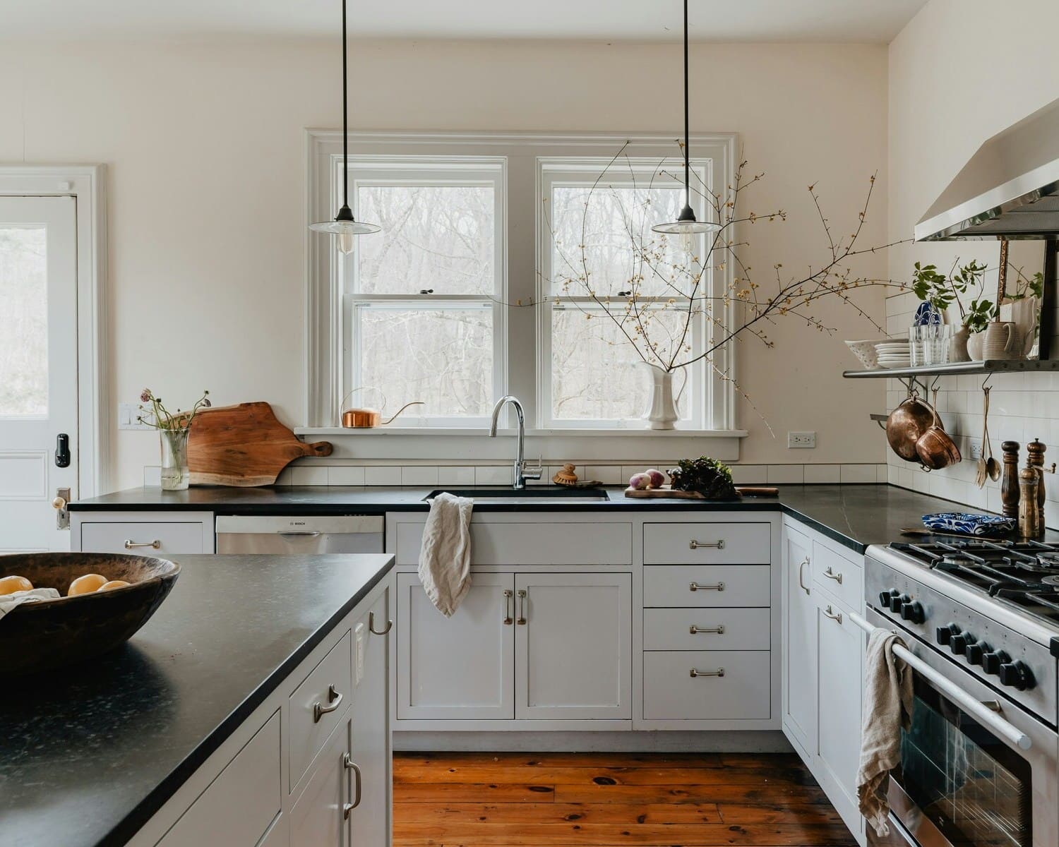 Rustic kitchen design with white cabinetry, dark countertops, and a minimalist black pendant light. The natural wood floor and decorative cutting board add warmth to the cozy space.