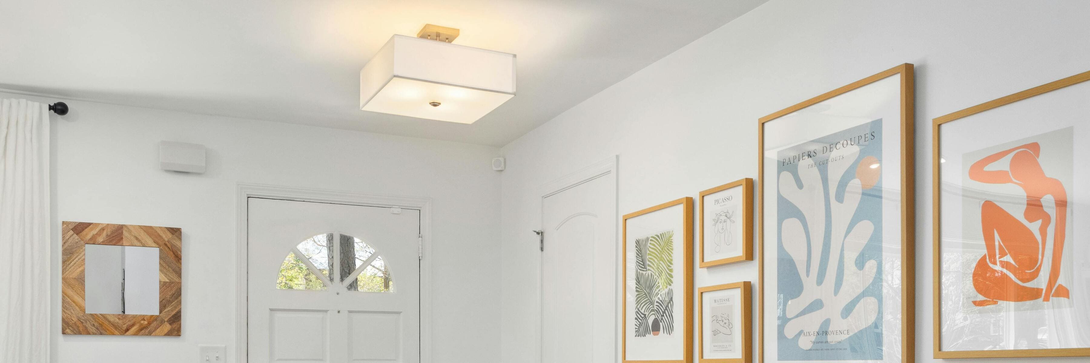 Square flush mount light in a stylish entryway with framed artwork and a wooden mirror.