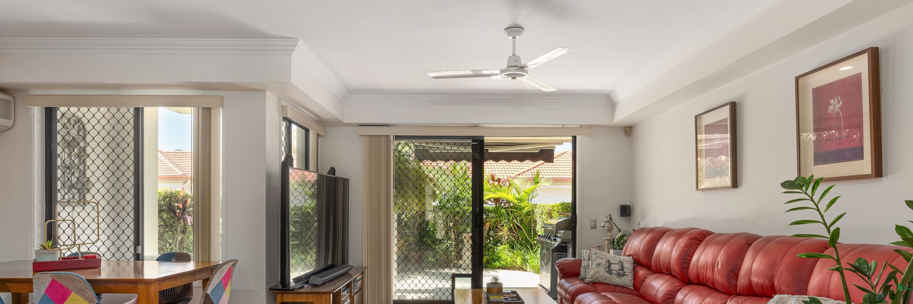 White ceiling fan in a contemporary living room featuring a red leather sofa and sliding glass doors leading to a garden.